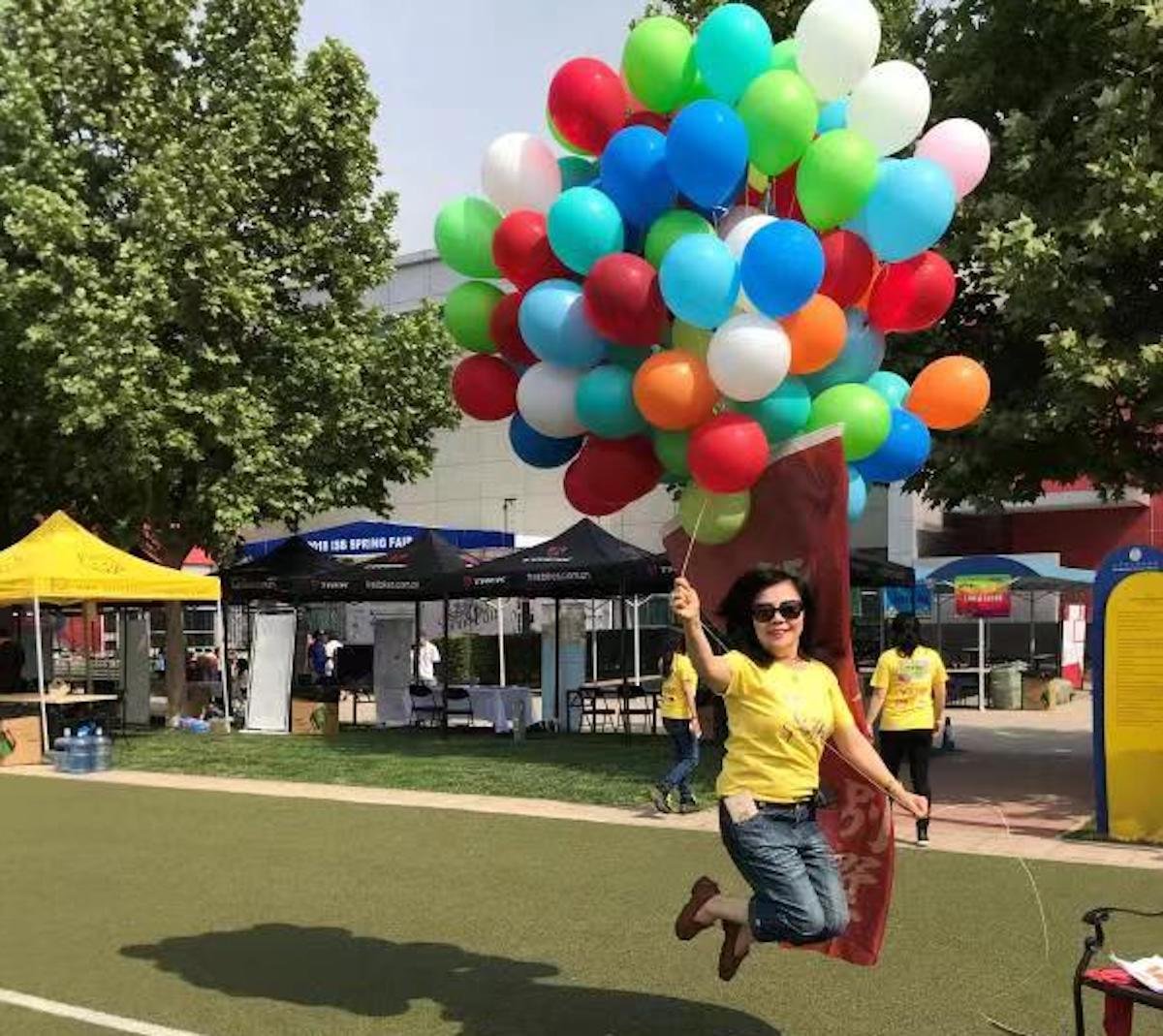 Xiu Mei Zhang leaping while holding some balloons at a fair