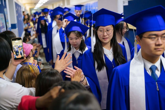 High School students parade in graduation gowns, high-fiving younger students
